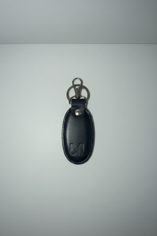 A dark navy blue leather keychain cover with a silver-tone metal clasp and keyring, featuring an embossed logo on the front, shown on a plain light background.